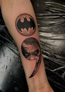 black and gray comic emblem and portrait forearm tattoo jeff thibodaux tattootopia