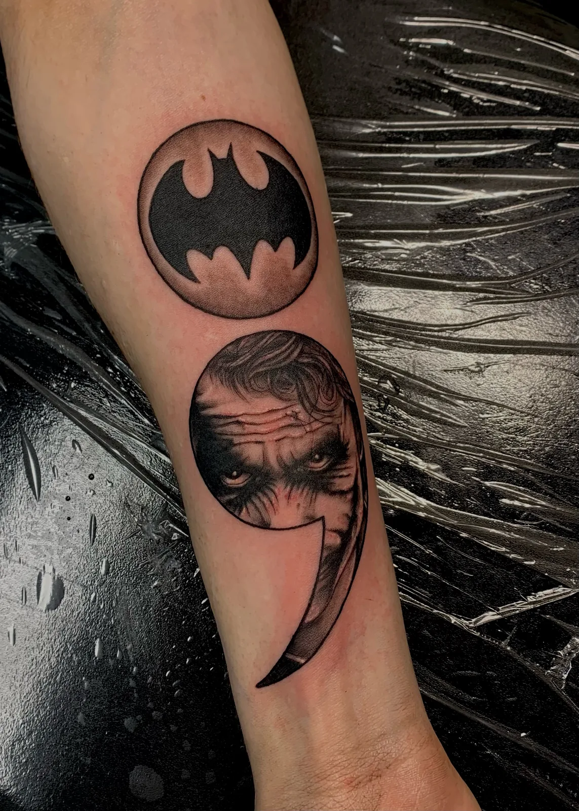 black and gray comic emblem and portrait forearm tattoo jeff thibodaux tattootopia